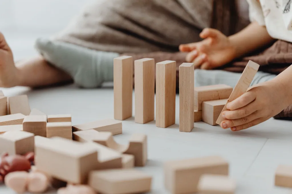 La main d’un enfant pose un cube en bois sur une petite construction
